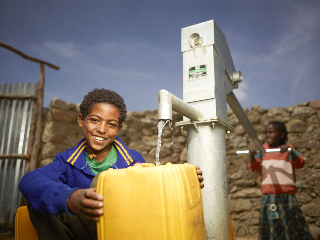 Jugendliche tanken aus einem neu installierten Brunnen von Charity: Wasser