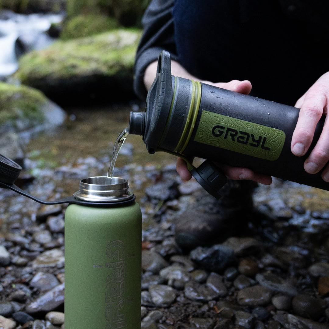 jemand schüttet Wasser aus der Tülle seines Grayls in eine andere Wasserflasche