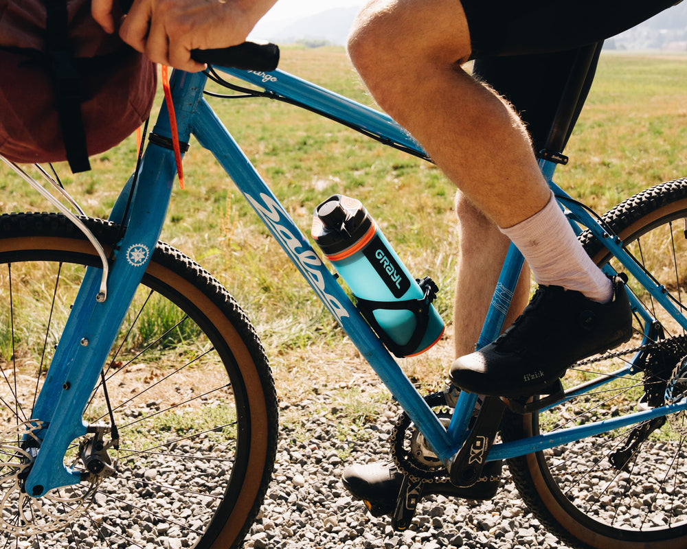 s'insère parfaitement dans le porte-bidon Arundel® Adjustable Looney Bin. Bali Blue GeoPress sur un vélo de gravier au bord d'une rivière.